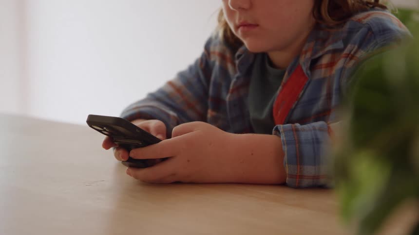 Child types on a smartphone on a wooden table