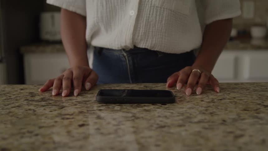 Person picks up a smartphone resting on a granite countertop