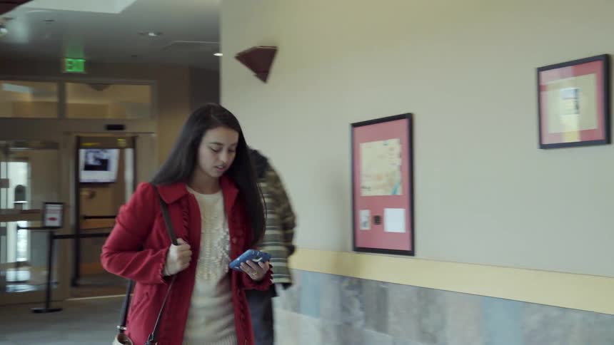 Woman walking inside building while looking down at cell phone