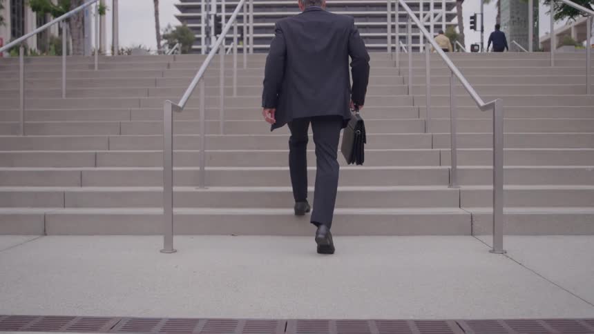 Man in a suit walks up a staircase carrying a black briefcase