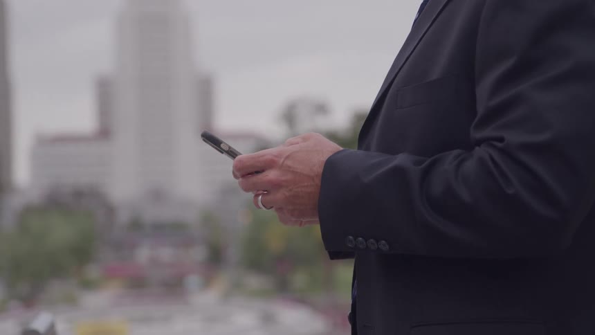 Man standing downtown texting on his phone with a tall building in the distance
