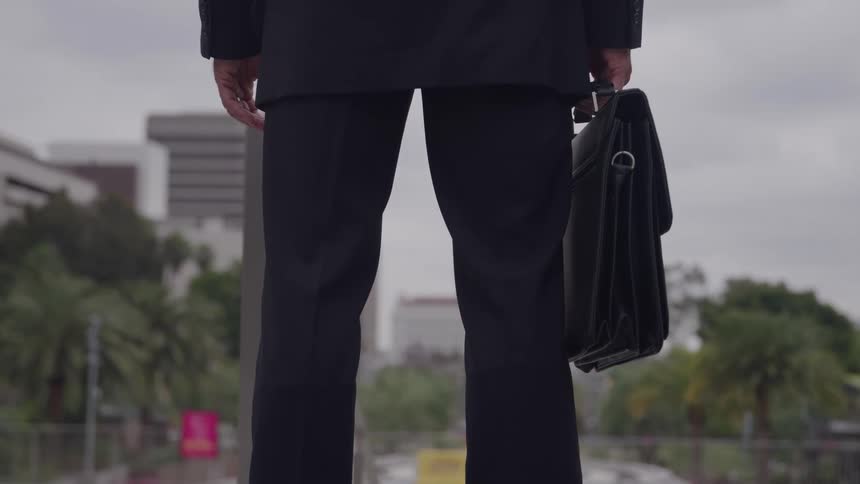 A businessman in a suit stands holding a briefcase against a blurred city background