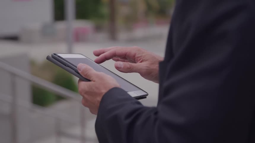 A businessman in a suit scrolls on a foldable smartphone outdoors