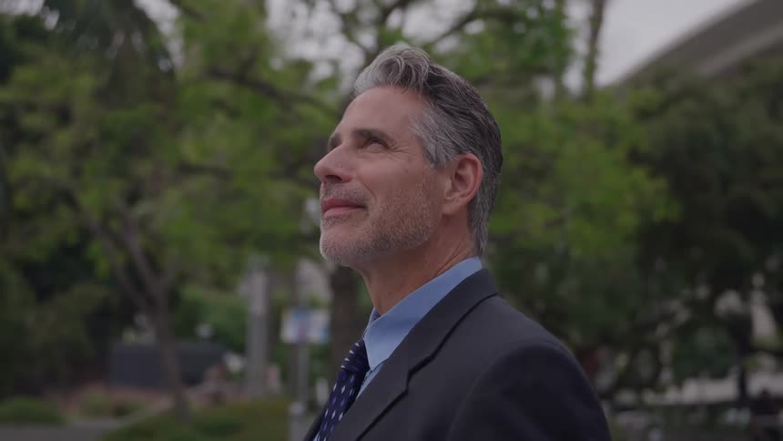 Man in a suit looking upward in a treefilled outdoor area