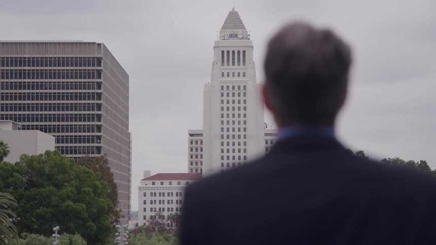 A man stands and looks out over city hall and the surrounding city skyline on an overcast day