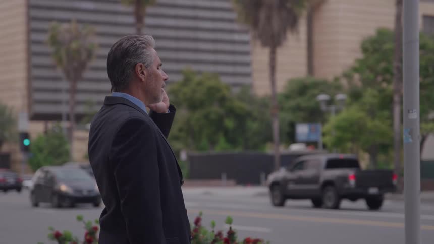 The man talks on his cell phone as cars pass by
