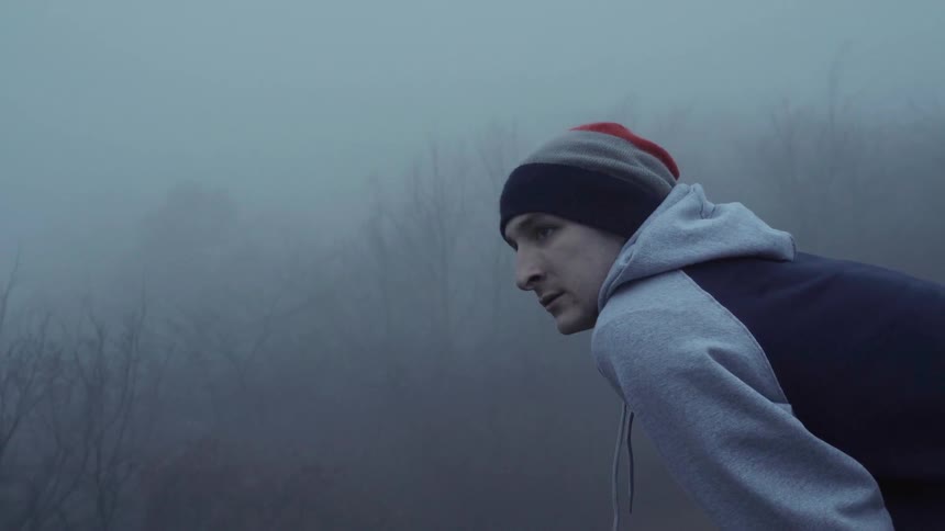 A man bending over and standing up straight in a foggy wooded area