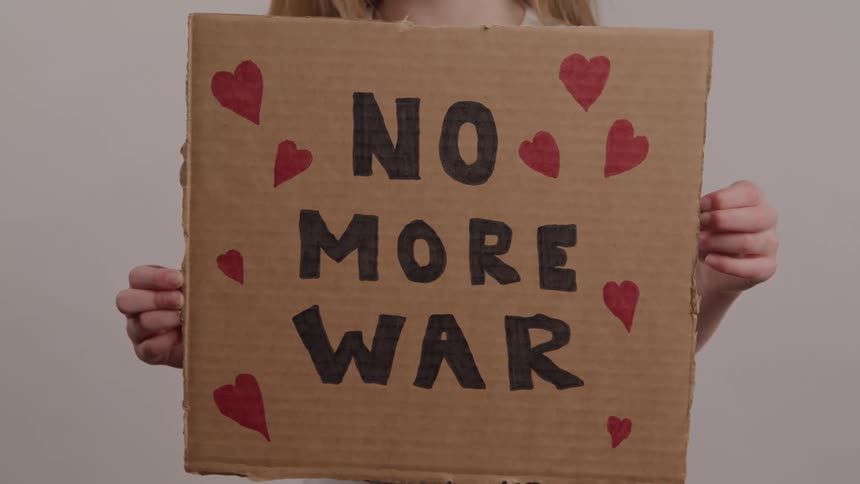 A child holds a handmade cardboard sign with the phrase no more war written on it and decorated with red hearts conveying a message of peace