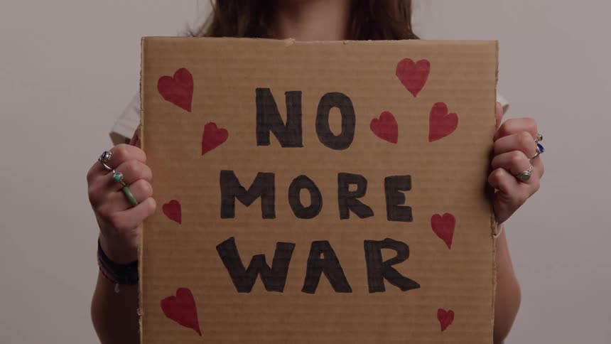 Person holds a cardboard sign with the phrase no more war decorated with red hearts