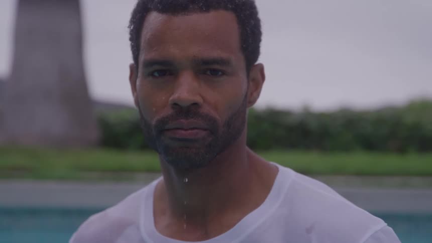 Man with a wet shirt stands in a pool with water dripping from his chin