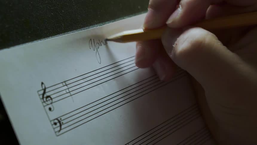 A person writes a title on a blank music sheet