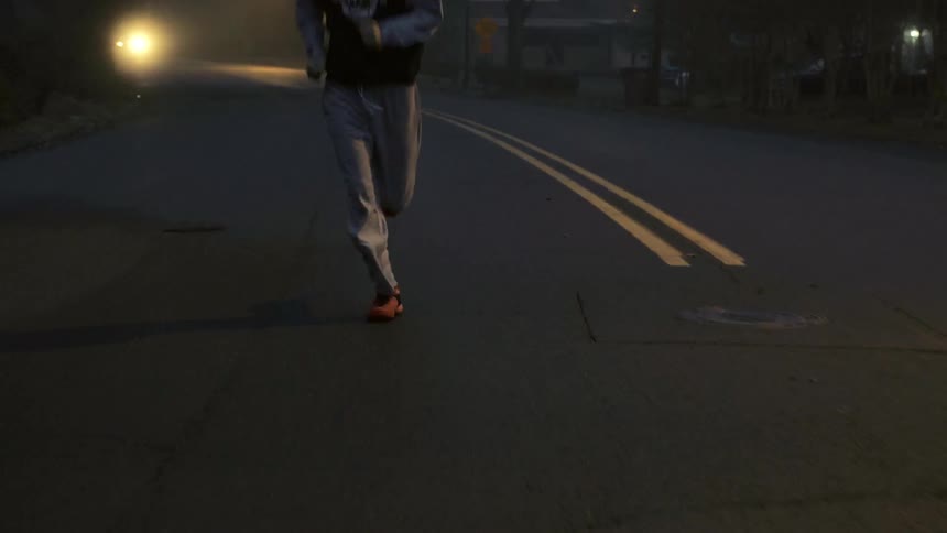 A young man is jogging in a suburban area at dusk or dawn