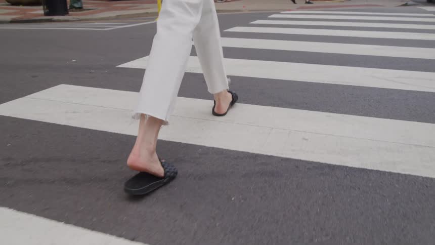 Person crosses a crosswalk wearing white pants and black sandals