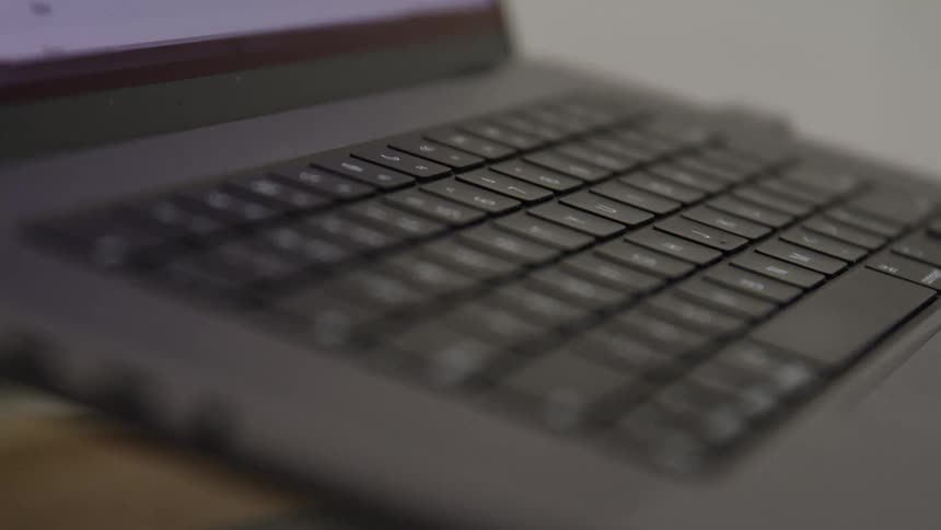 A laptop computer with a black keyboard rests on a wooden desk indoors