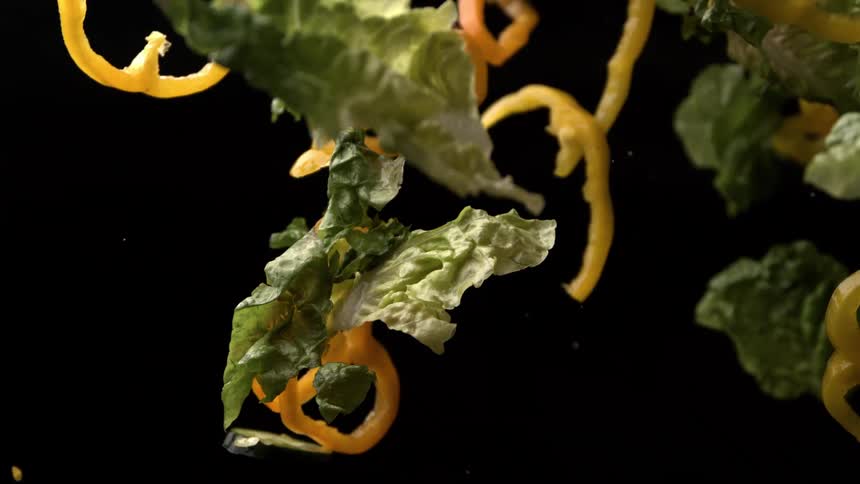 Lettuce leaves yellow bell peppers and cherry tomatoes appear suspended against a black background