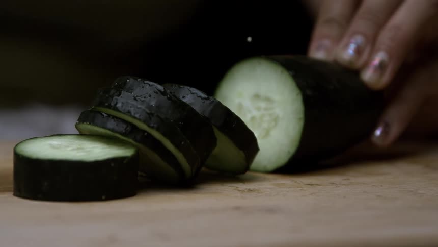 Woman slicing a cucumber on a chopping board with a big knife