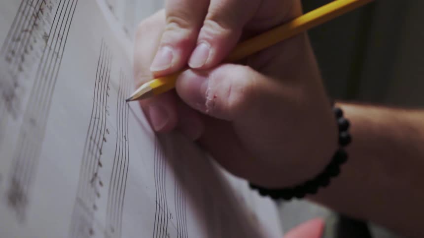 Person writes music notes on a piece of paper