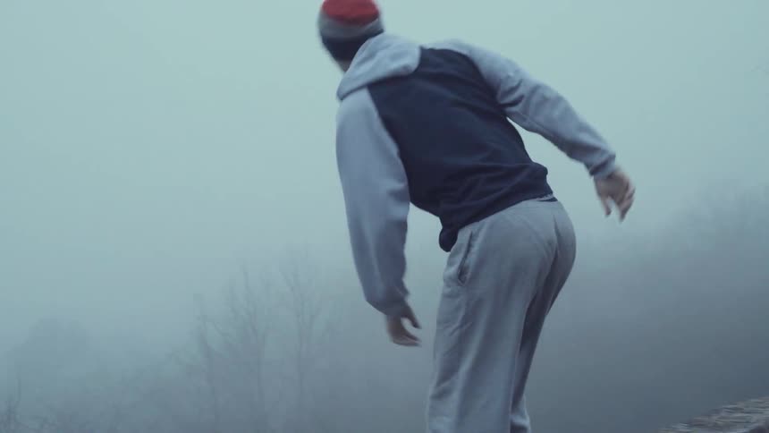 A jogger climbs up onto a rock ledge on a foggy day