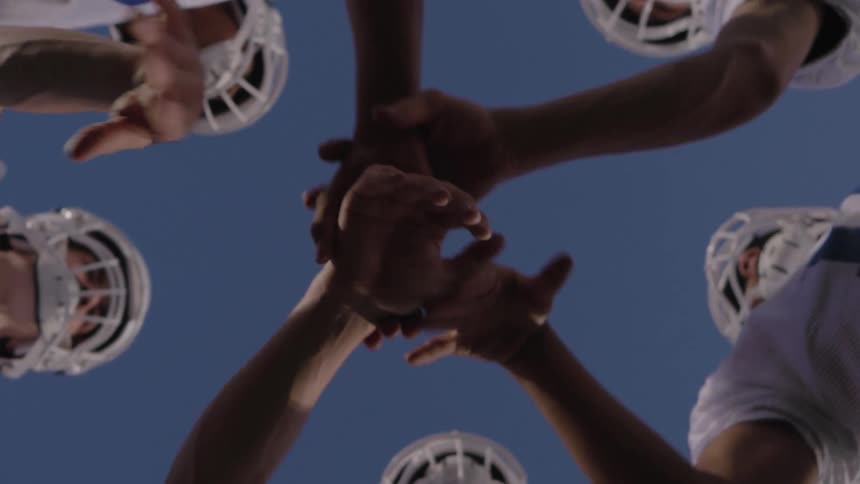 Football players touch hands in a team cheer during the day