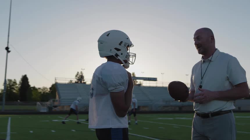 The couch is talking with a football player on the field