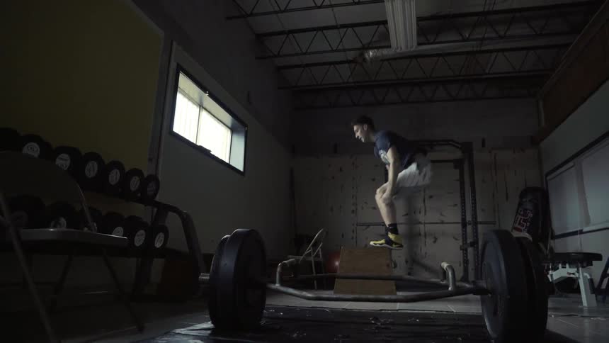 A man jumps onto a box repeatedly in a gym