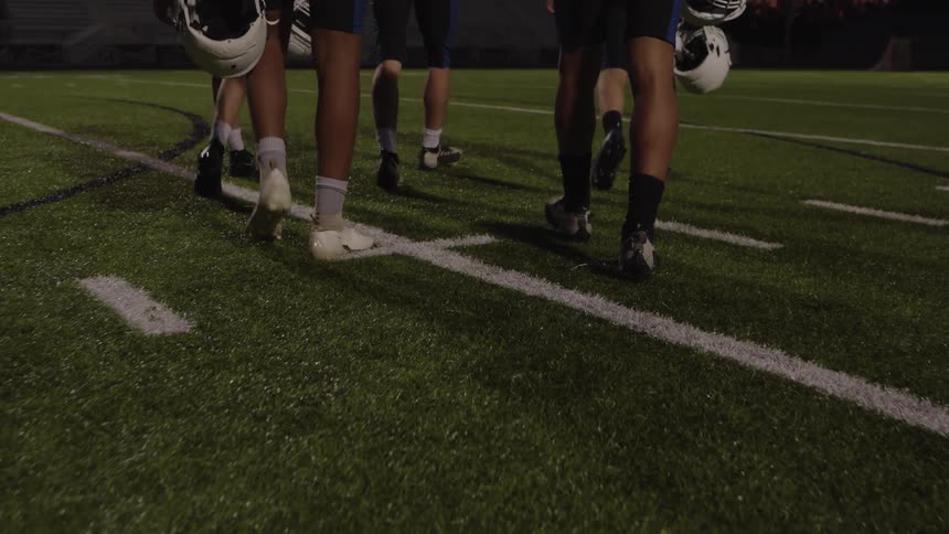 Football players carry their helmets as they walk across the field