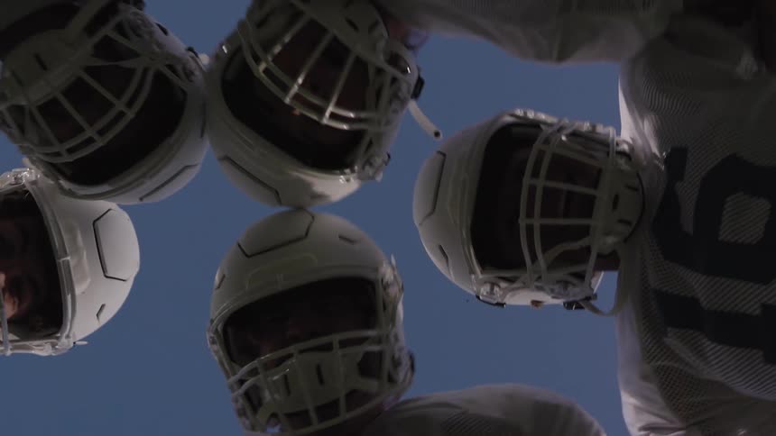 American football players gathered in a circle looking down