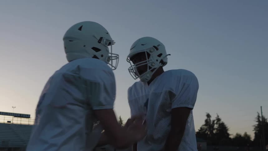 Two football players face off at dusk locked in a moment of tension and focus under stadium lights