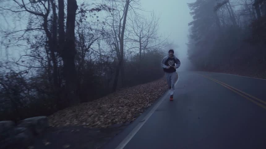 Man jogging on a tree lined road on a foggy day