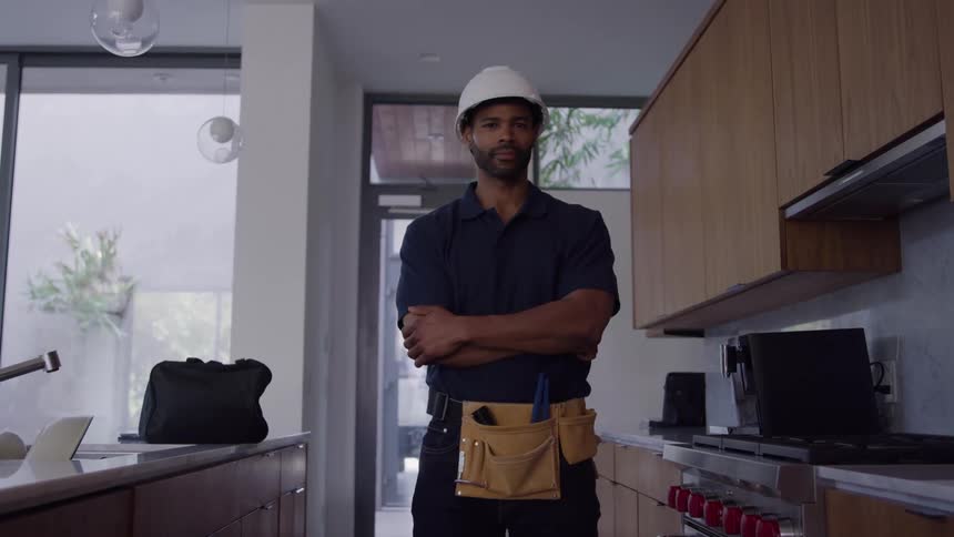 Construction worker wearing a white helmet and blue clothes standing on a kitchen indoors during day time