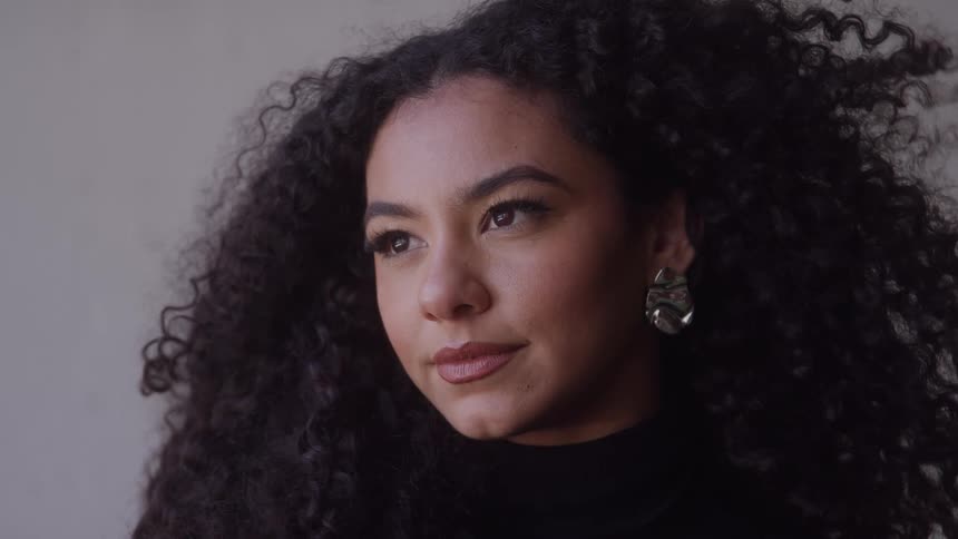 Woman with long curly hair looks to the side wearing a black sweater and metallic earring