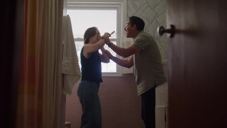 A woman and a man are in a pinktiled bathroom nervously waiting for the result of a pregnancy testthe woman holds up the test they both excitedly react with shouts and laughter and then embrace in a joyful hug