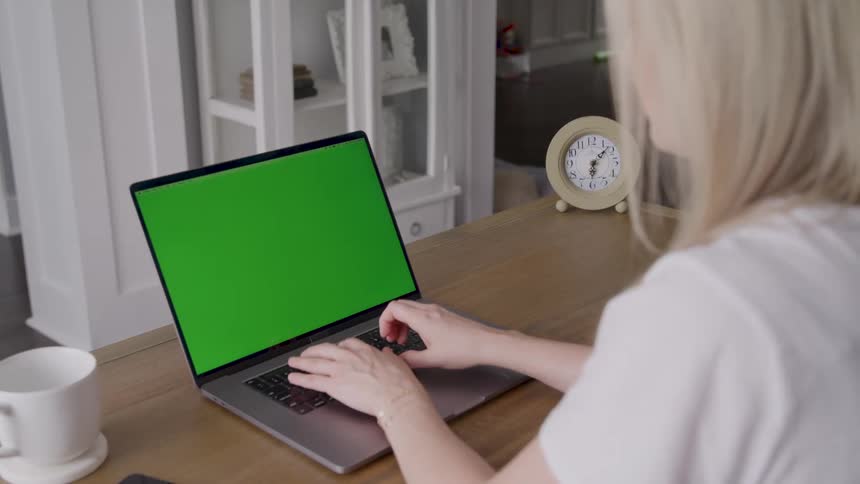 Young female person typing on a laptop computer showing a replaceable screen over a wooden desk indoors during day time