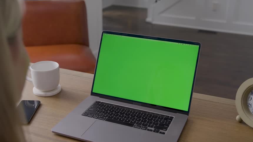 Person looks at a laptop on a table beside a cup and a clock