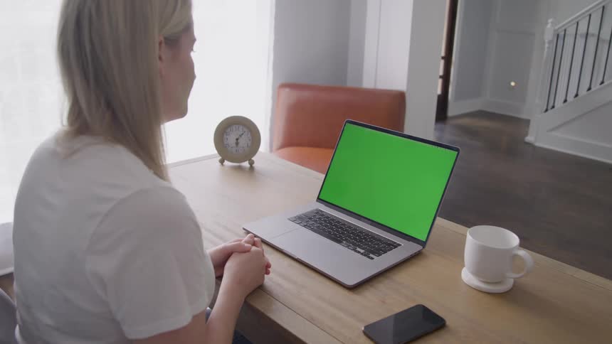 Woman sitting at a table in front of a laptop computer as she talks and waves