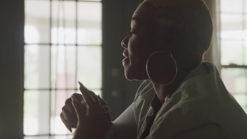 Woman in profile gestures while speaking in an indoor setting lit by windows