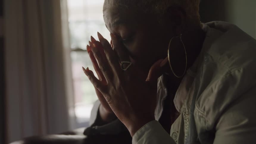 Close up portrait of a black woman praying while sitting indoors during daytime