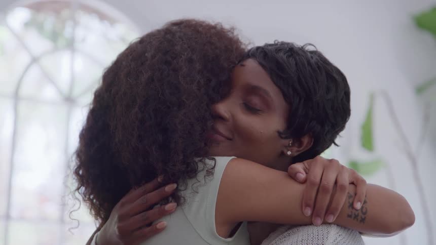Two people embrace with a calm expression in a welllit room