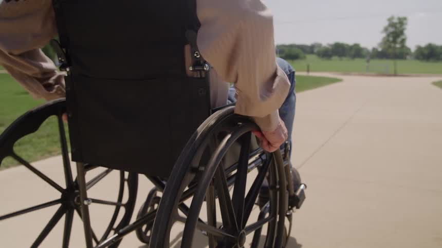 Close up of a man rolling his wheelchair along a pathway outdoors during daytime