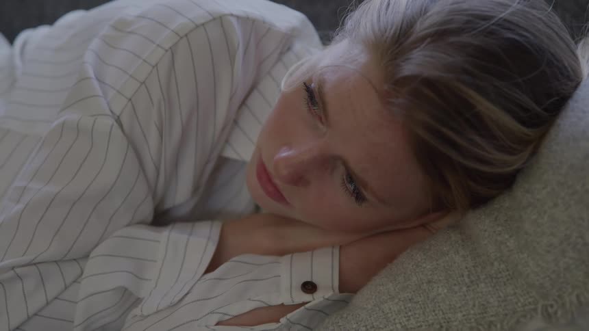 A woman from the waist up with hands together under her head is wearing a striped shirt is laying on her side on a gray pillow
