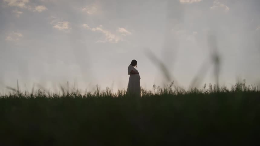 Pregnant woman walks in a field with the horizon in the background