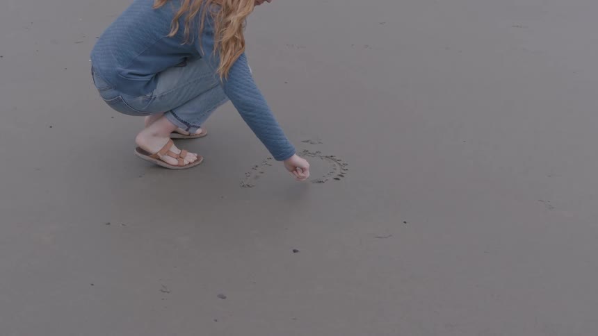 A female teenager drawing a heart on wet sand at the beach during daytime