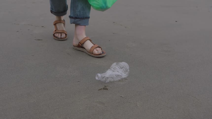 Adult woman picking up liter from a beach outdoors during day time