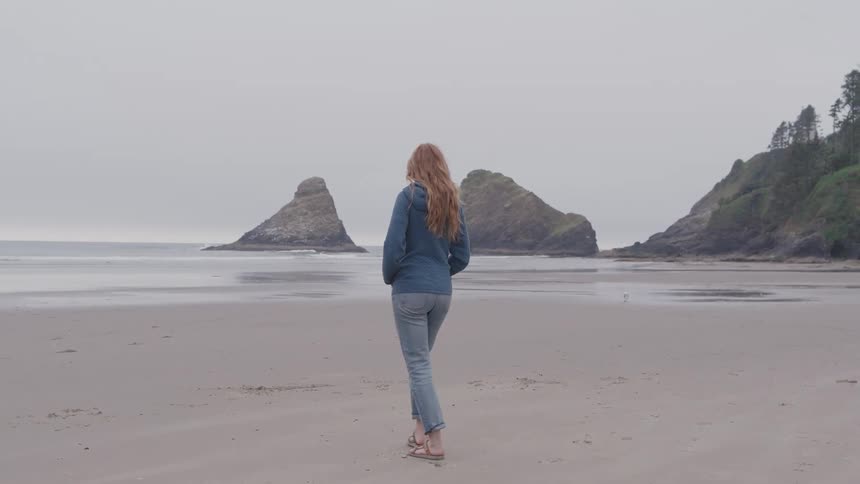 Woman walks barefoot across sand toward the sea
