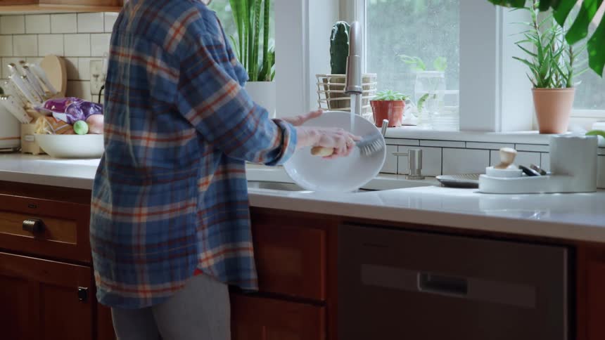 Person washes dish at kitchen sink lit by natural light