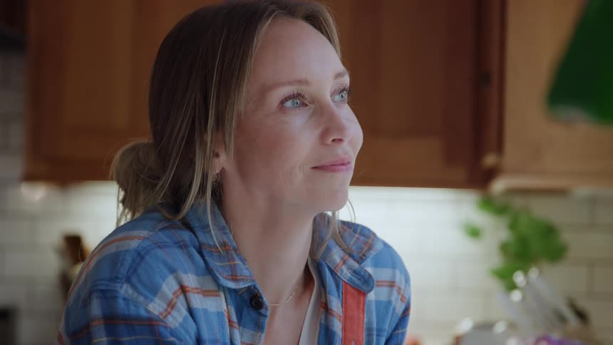 Woman looks at something offframe in kitchen lit by natural light