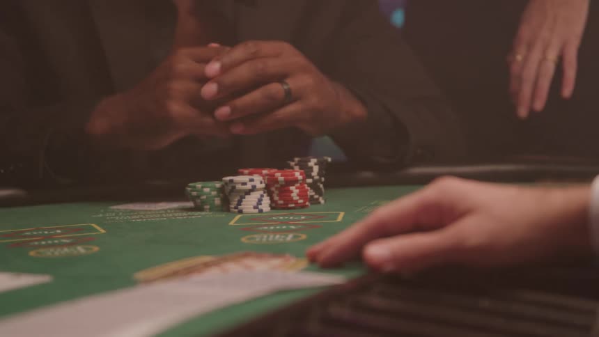 Hand stacking red white and blue chips on green table with printed betting areas