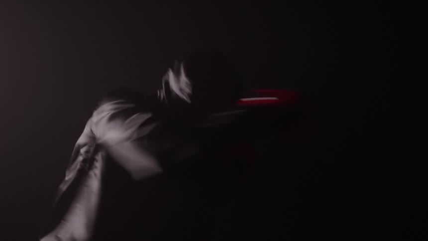 Shrouded in darkness a hooded boxer throws a rapid succession of punches their red gloves creating streaks of motion in the dim light