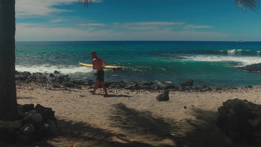 Man walking on the beach carrying a surfboard