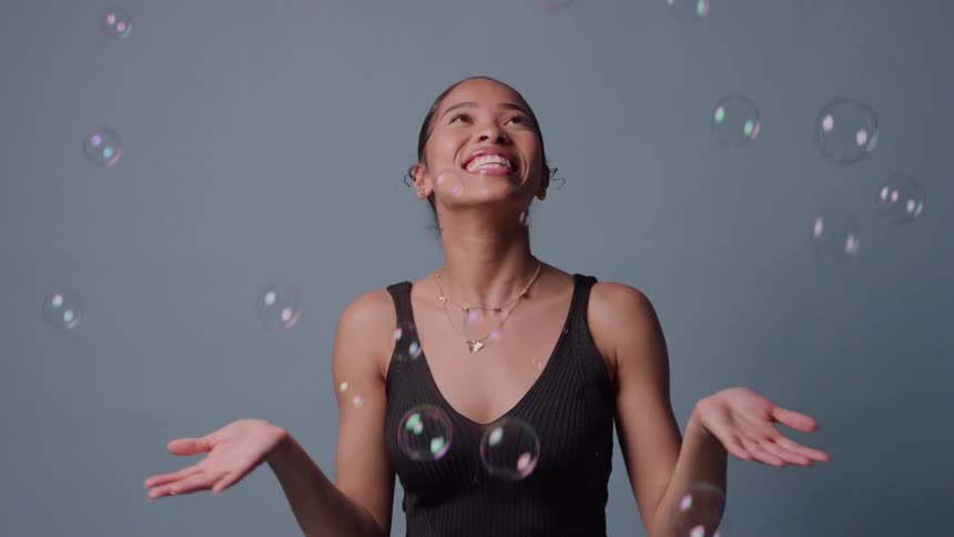 Woman smiles with arms raised as soap bubbles float around